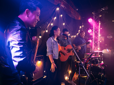 Music band performing on stage at the concert, having a singer singing song and team playing musical instruments in the club.