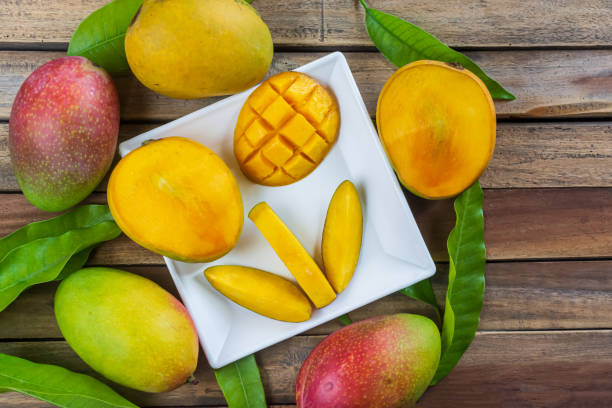 istock Fresh and ripe mango fruit in a white plate with green leafs on wood background. 1328190508