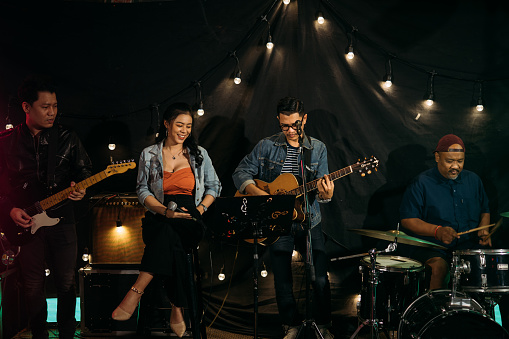 A young adult  caucasian female singer passionately recording a song in a cool recording studio. The female singer is attractive and wears casual clothes. The studio is full of audio and recording equipment. There is a microphone stand, a music stand and some drums. There is a beautiful orange light illuminating the room.