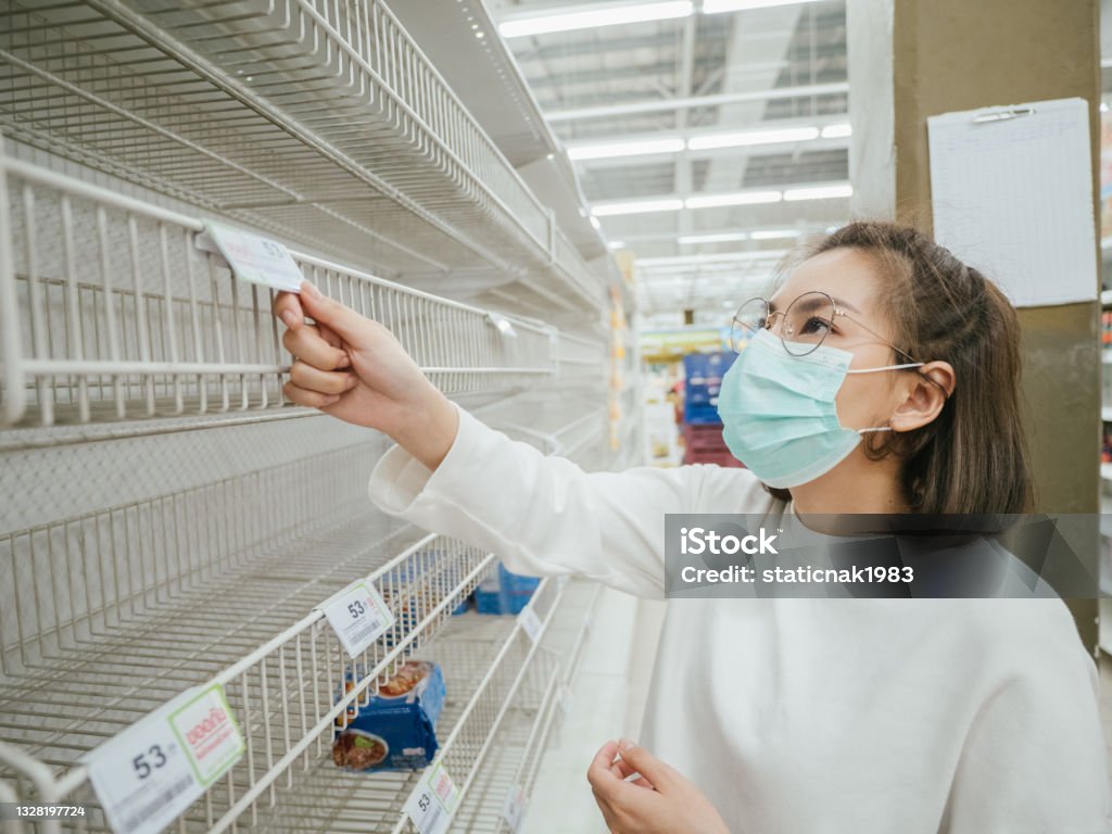 Young Woman in Medical Mask Shopping During Empty Shelf. Young asian woman wearing mask and reading label on empty shelf in Supermarket in Bangkok, Thailand. Empty Stock Photo