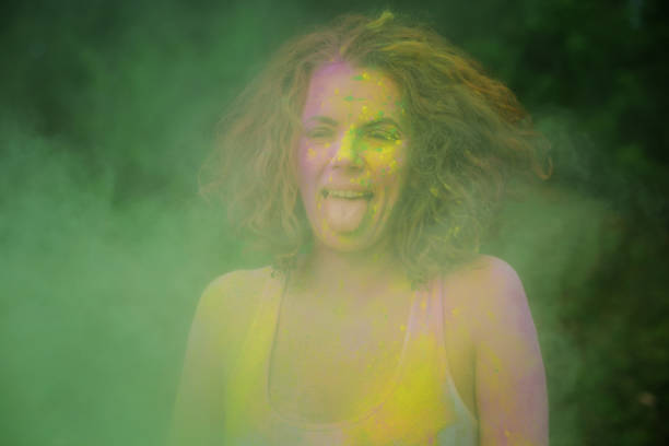istock Positive redhaired model wearing white t shirt playing with green dry Holi paint exploding around her 1328198491