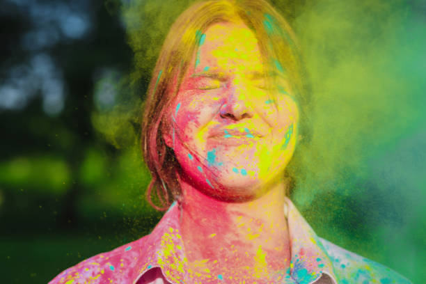 istock Amazing brunette model with short hair posing with exploding yellow and green Holi paint in the park. Empty space 1328198525