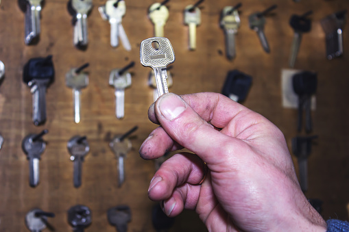 The master holds the key against the background of other blanks for making copies of keys