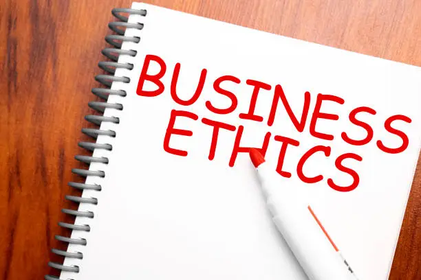 Photo of Text BUSINESS ETHICS written in notepad, Office wood table and red marker from above, concept image for blog title or header image. Aged vintage color look.