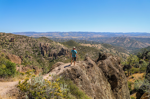 Man standing on rock ledge  overlooking  the landscape of Pinnacles National Park in California