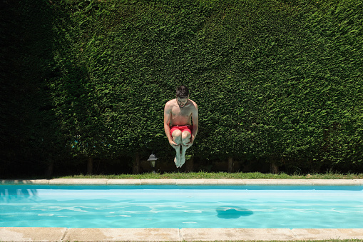 Young man cannonball jumping into a swimming pool. Summer concept.