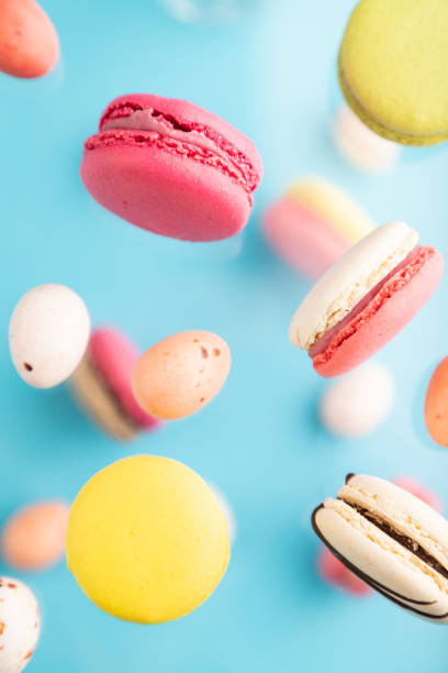 istock Multicolored flying macaroons and chocolate eggs frozen in the air on blurred blue background. top view, flat lay, close up. Breakfast, morning, concept. 1328209873
