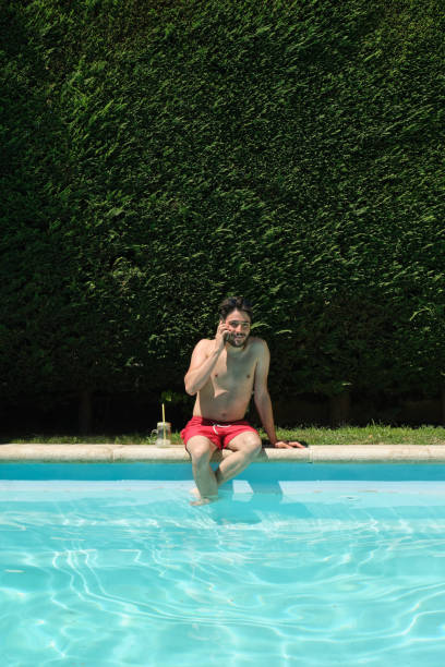 istock Digital nomad talking on his smartphone sitting on the swimming pool edge. Summer concept. 1328209943