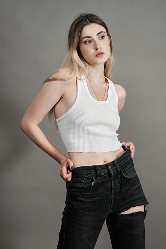 young woman in torn jeans stand on a gray background