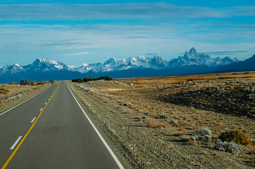 Road to Perito Moreno Glacier, Patagonia, Argentina. View of a road and arid landscape with snow-capped mountains on the horizon.