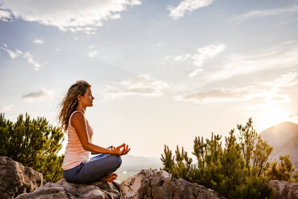 junge frau preformt yoga in den bergen bei sonnenuntergang - zen like nature breathing exercise sitting stock-fotos und bilder