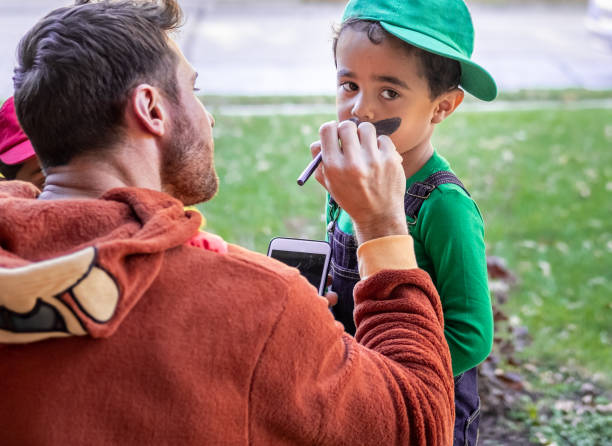 White father dressed up for Halloween painting mustaches on his African American son's face White father dressed up for Halloween painting mustaches on his African American four-year old son's face halloween face paint stock pictures, royalty-free photos & images