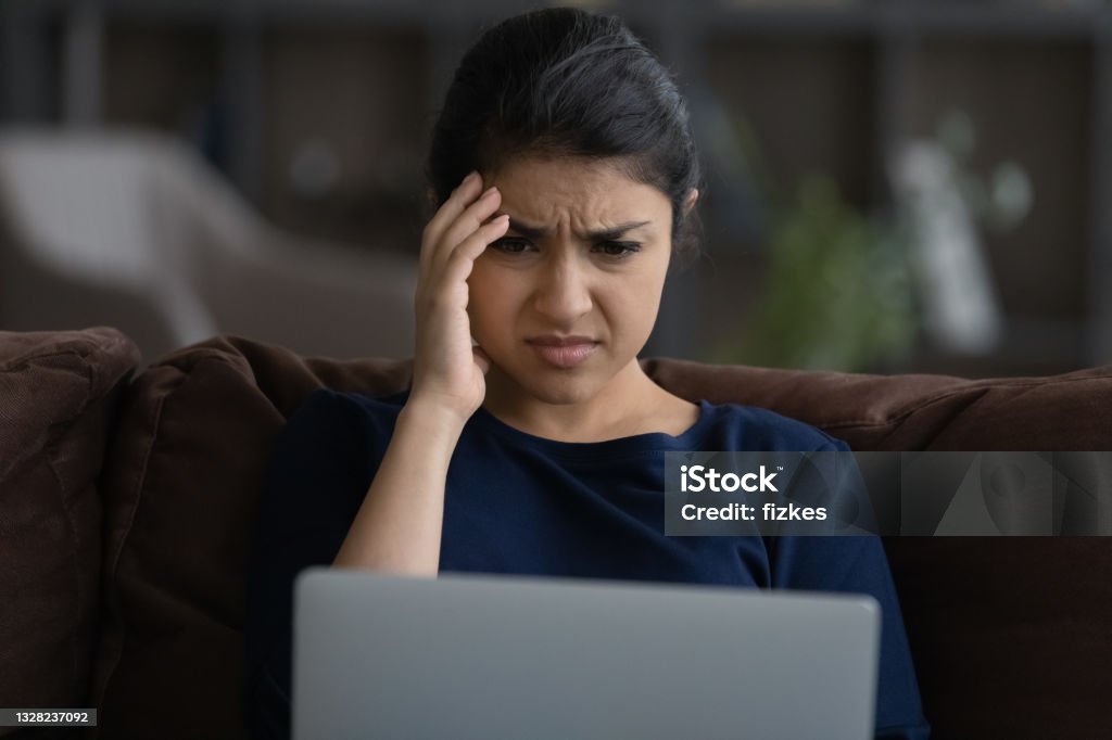 Close up unhappy Indian woman looking at laptop screen Close up unhappy Indian woman looking at laptop screen, reading bad news in message or social network, sitting on couch at home, worried businesswoman freelancer received dismissal notification Negative Emotion Stock Photo