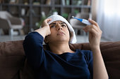 Close up sick Indian woman feeling unhealthy, holding thermometer