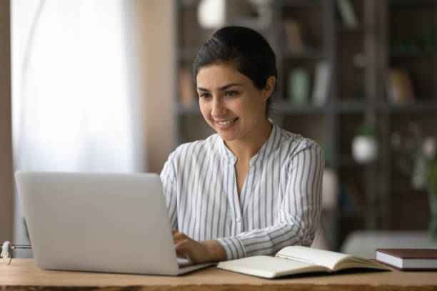 istock Smiling Indian woman using laptop, studying online at home 1328237141