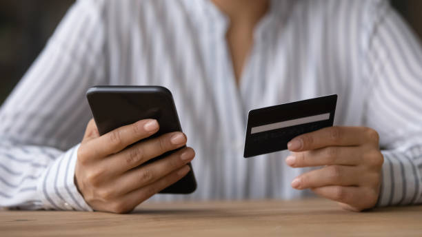 Close up woman paying online by credit card, using smartphone Close up woman paying online by credit card, using smartphone, sitting at wooden desk, young female holding phone, browsing banking service, checking balance, shopping, making internet payment scammer stock pictures, royalty-free photos & images