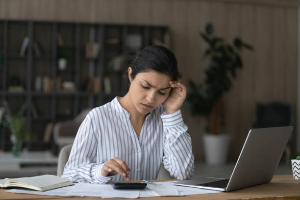 istock Unhappy Indian woman checking domestic bills at home, using calculator 1328237174
