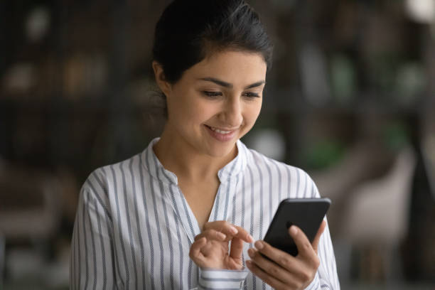 istock Close up smiling Indian woman using smartphone, looking at screen 1328237181