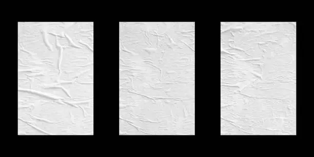 Photo of white crumpled and creased glued paper poster set isolated on black background