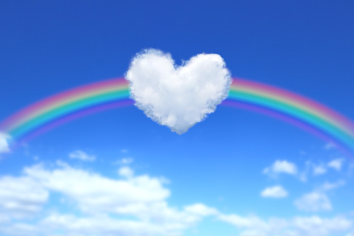 There is a big heart-shaped cloud floating in the sky, and a big rainbow behind it.