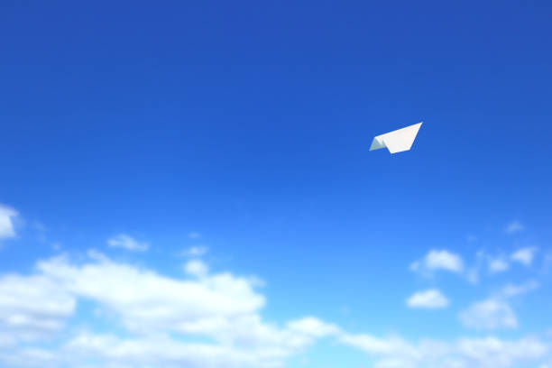 A paper airplane flies freely in the clear blue sky.