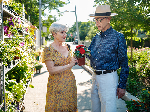 Senior couple buying flowers at the local flower shop. Both nicely dressed in summer outfit, woman wearing summer dress, man wearing eyeglasses, shirt and khaki pants and Panama hat. Outdoor location of urban small flower business in summer time.