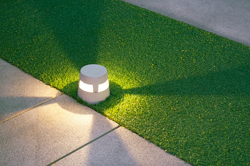 Illuminated LED ground lantern on artificial turf and gravel stone walkway in the evening park