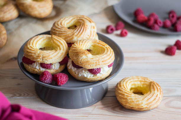 istock Cream puff rings eclairs choux decorated with fresh raspberries on grey plate, selective focus 1328253030