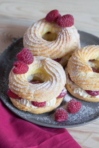 istock Cream puff rings eclairs choux decorated with fresh raspberries on grey plate, selective focus 1328253037