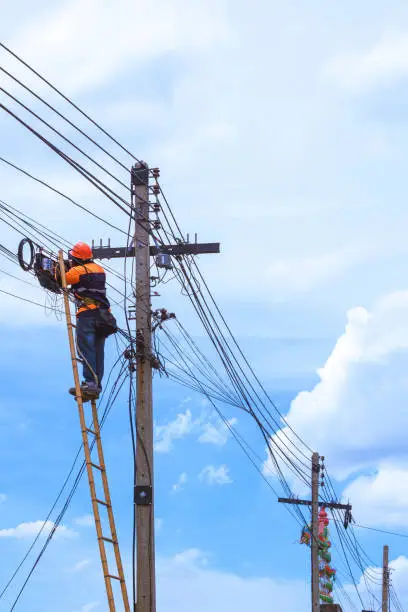 Photo of technician on wooden ladder checking fiber optic cables in internet splitter box on electric pole against cloudy sky