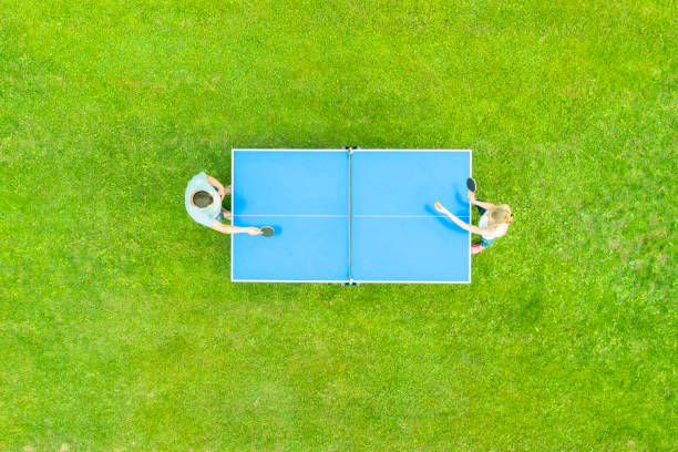 вид с воздуха людей, играющих в пинг-понг матч на открытом воздухе. вид сверху мужчина и женщина играют в настольный теннис на зеленой травя� - table tennis table стоковые фо�то и изображения