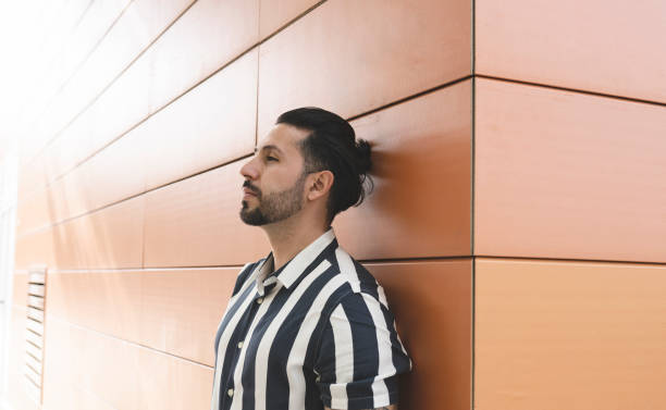 istock man with ponytail and tattoos leaning on a wall 1328271145