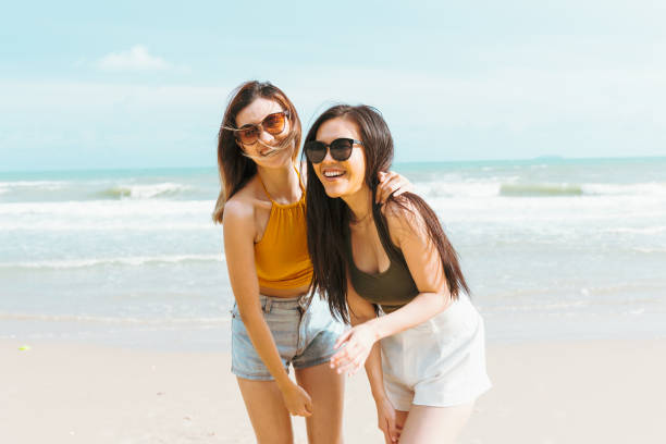 Two Asian women friends in summer casual clothes Take a photo together at the beach on vacation in tropical country. Young beautiful Female joy in the beach on a sunny day stock photo
