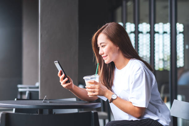 istock A beautiful young asian woman holding and using mobile phone while drinking coffee in cafe 1328275651