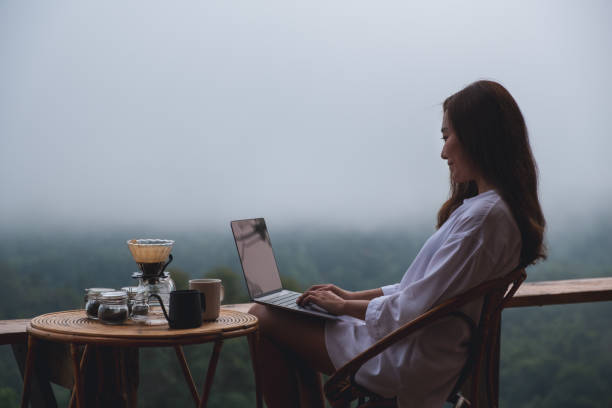 istock A woman using and working on laptop computer while sitting on balcony with a beautiful nature view on foggy day 1328275662