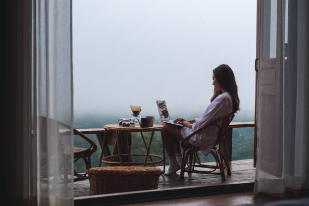 istock A woman using and working on laptop computer while sitting on balcony with a beautiful nature view on foggy day 1328275700