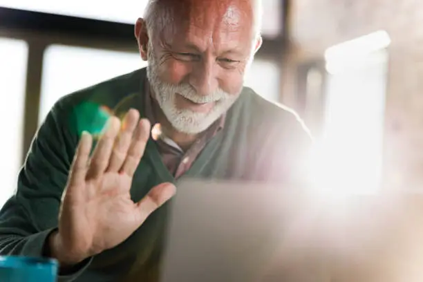 Happy mature man greeting someone during a conference call over computer at home.