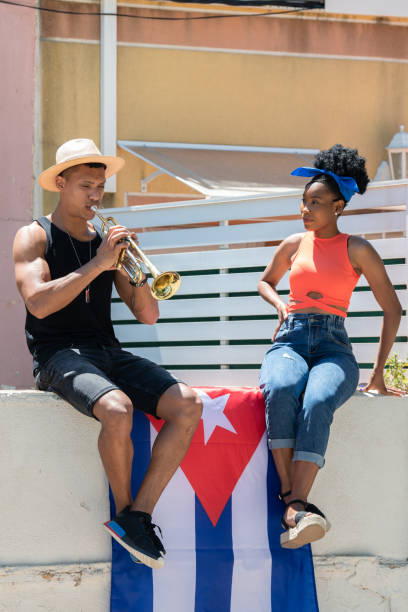 latina-frau beobachtet einen latino-mann, der eine trompete spielt, die an einer wand mit der kubanischen flagge sitzt: musikkonzept. - straßenmaler stock-fotos und bilder