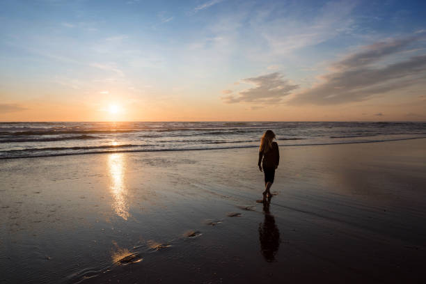 istock young girl walking alone on the beach at sunset 1328278119