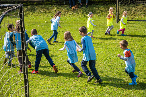Young boys and girls running in circle between two goals on playground. Children team sport on fresh air, physical activity and entertainment.