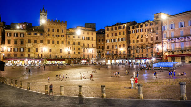 A suggestive night scene of Piazza del Campo in the historic and medieval heart of Siena in Tuscany A stunning and suggestive evening view of Piazza del Campo in the historic heart of the medieval city of Siena, in Tuscany, central Italy. Center of the ancient medieval city since 1169, the Piazza del Campo or simply the Campo is one of the most beautiful and famous squares in the world for its particular shell shape. In this space every year the seventeen historical districts of Siena compete in the Palio, one of the oldest horse races in the world. In the background the white bell tower of the Cathedral or Duomo. Siena is one of the most beautiful Italian cities of art, in the heart of the Tuscan hills, visited for its immense artistic and historical heritage and for its famous popular traditions. Since 1995 the historic center of Siena has been declared a World Heritage Site by UNESCO. Image in high definition format. siena italy stock pictures, royalty-free photos & images