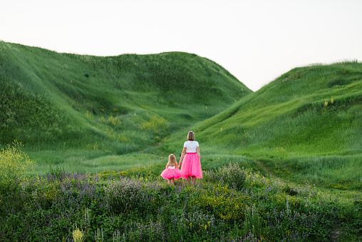 Mom with daughter in pink dresses walking in mountains. Mother with a daughter in the same clothes. Family same look. Clothing for parent and child. Family holiday together in nature. Back view.