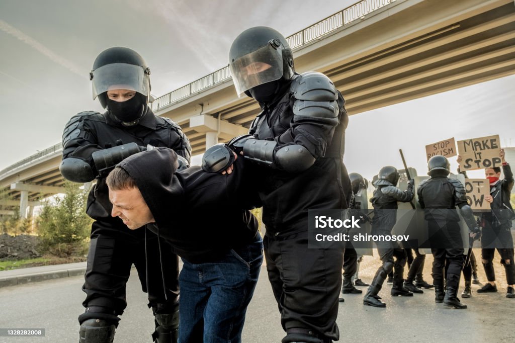 Riot police twisting man at rally Riot police in body armors twisting man into uncomfortable position while confronting crowd in city Russia Stock Photo