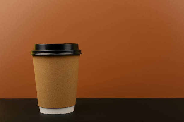istock Brown cardboard cup of coffee on black table against brown background with copy space 1328283418