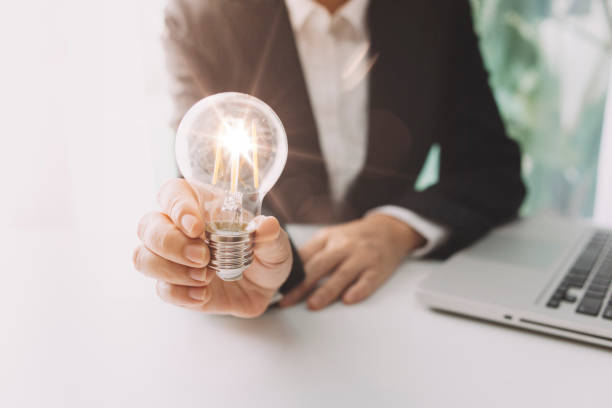 istock business hand holding lightbulb with using smartphone, laptop computer and money stack in office. idea saving energy and accounting finance concept in morning light 1328283733