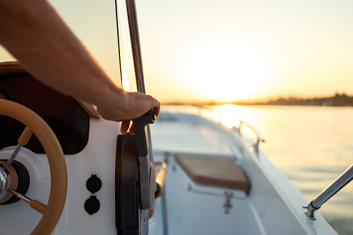 Close-up shot of a man's hand on a speedboat's steering wheel at sunset on the Danube river.