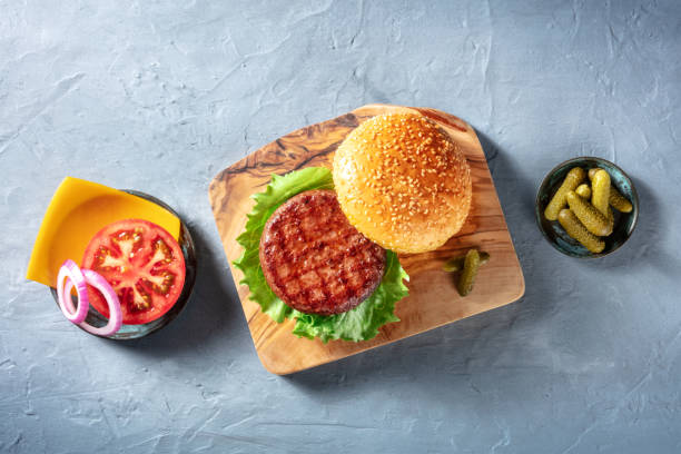 Burger ingredients. Hamburger beef patty, green salad leaf Burger ingredients. Hamburger beef patty, green salad leaf, Cheddar cheese, tomato and red onion, with pickles, overhead shot on a blue background spanish hamburger stock pictures, royalty-free photos & images
