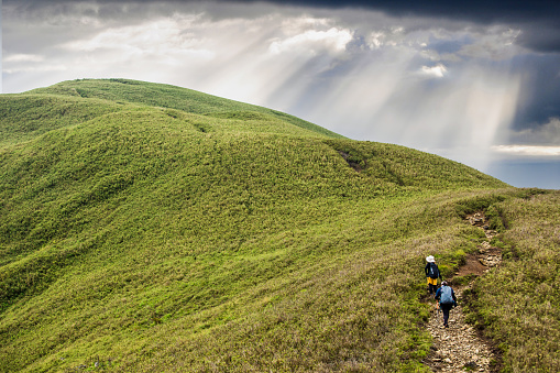 Two female hikers walk along a path winding its way up to a mountain summit.