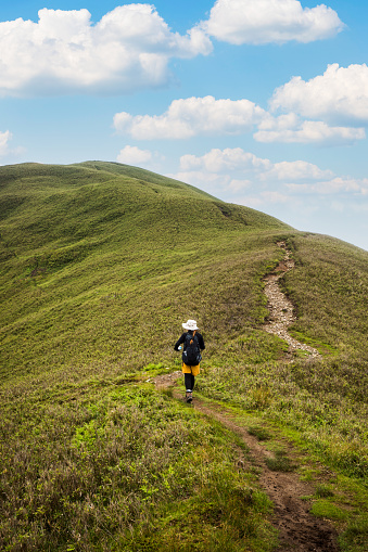 A single female hiker climbs her way up a path to a mountain summit on a sunny day.