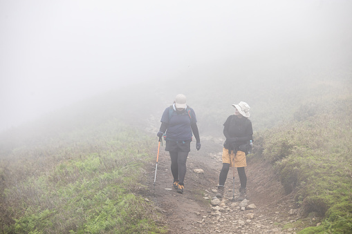 Two female friends hiking down a mountain path while clouds engulf the mountain reducing visibility to only a few meters.